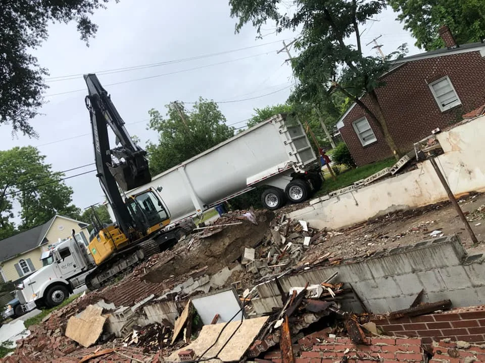 CASE excavator and the tri axle dump truck at a West Columbia teardown, with a broken out block foundation wall and concrete rubble spread across the lot