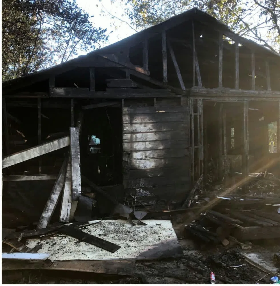 Burnt house with charred framing and roof standing before demolition
